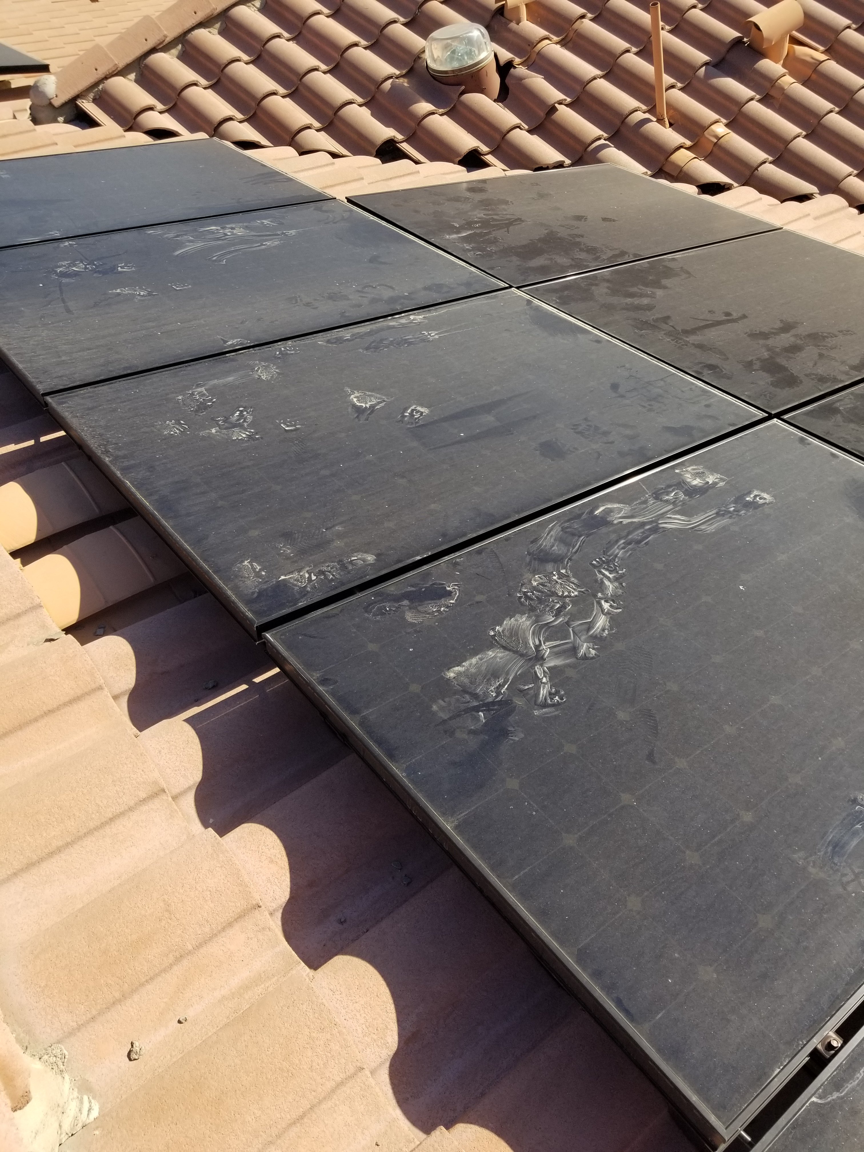 Side-by-side image showing water spots and mineral residue on a solar panel after sprinkler use compared to a clean, streak-free panel